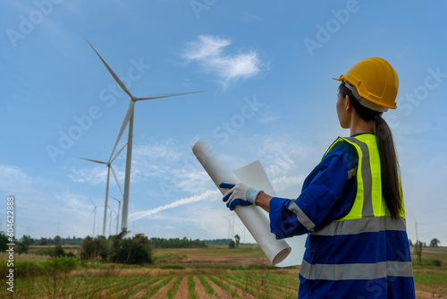 Woman worker Planning Contractor Checking at wind turbine construction at wind turbine at autumn cloudy sky green meadow outdoors