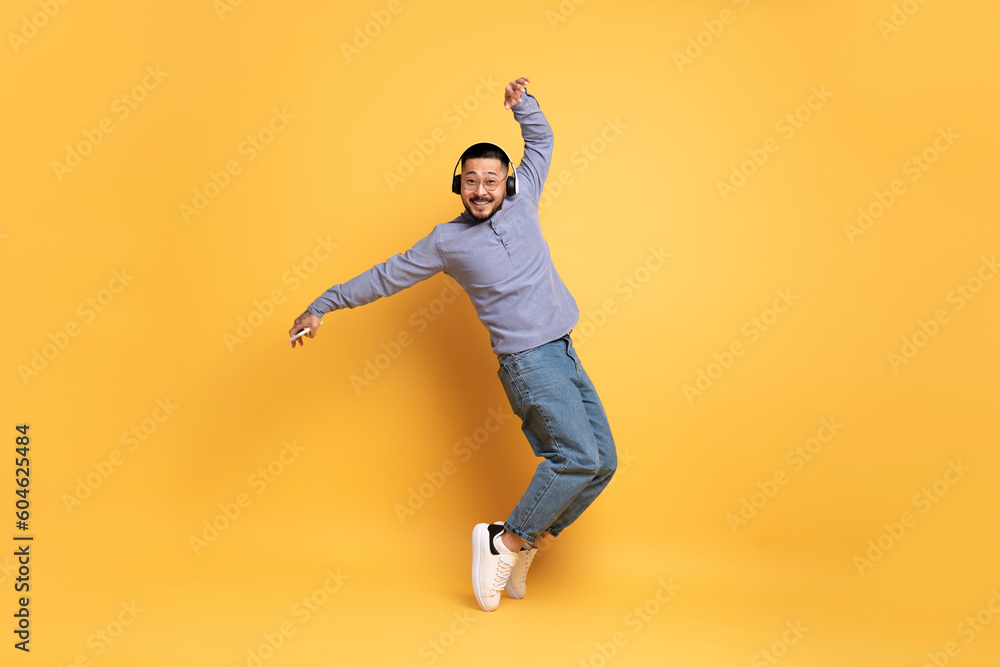Cheerful Asian Man Wearing Wireless Headphones Dancing Over Yellow Background