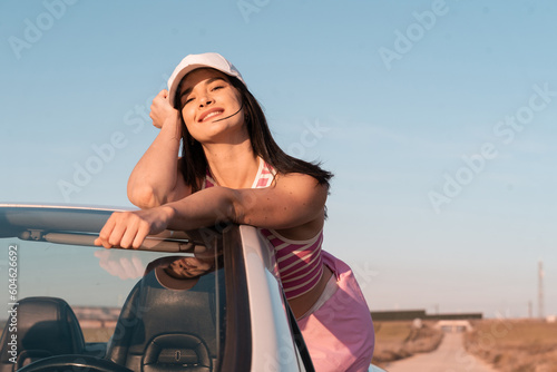 European girl dressed in pink smiling outdoors in her car on a highway during summer vacation -