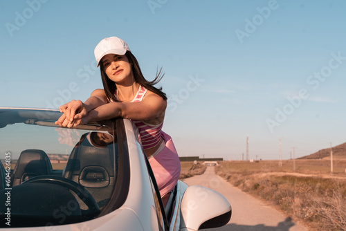 European girl dressed in pink smiling outdoors in her convertible car on a highway during a summer vacation - © Alberto Cotilla