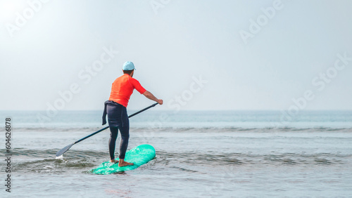 A healthy man paddling in the ocean like a SUP but in a green surfboard on a sunny day of summer while he enjoys its holidays