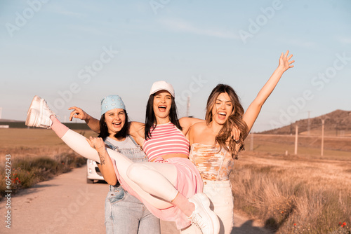 The three girls are having fun and smiling as they lift their friend, they are celebrating the arrival of summer.