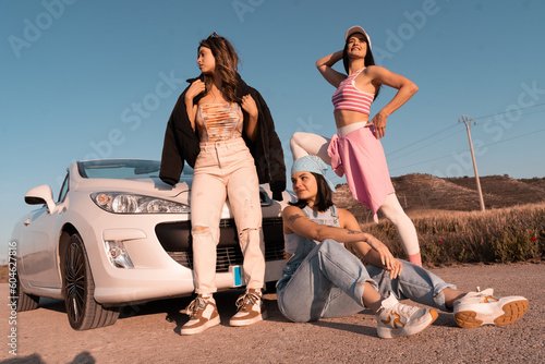The three friends pose with their white car during a summer trip.