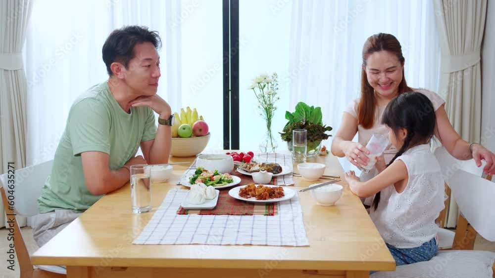 Happiness family with mother and adorable daughter drinking milk or beverage together in the living room at home, mom and dad eating food with kid, nutrition and healthy, lifestyles concept. Happiness family with mother and adorable daughter drinking milk or beverage together in the living room at home, mom and dad eating food with kid, nutrition and healthy, lifestyles concept.