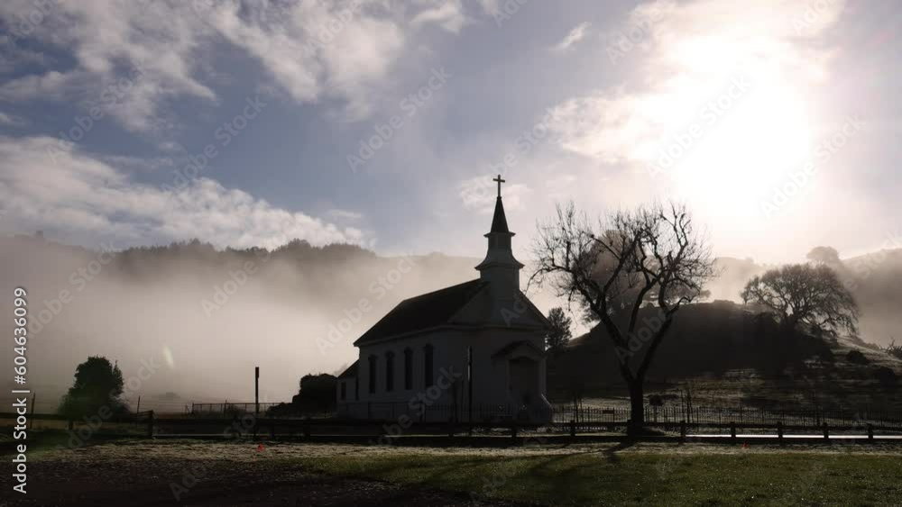 Early morning mist and fog with bright sun behind silhouetted church in countryside Early morning mist and fog with bright sun behind silhouetted church in countryside