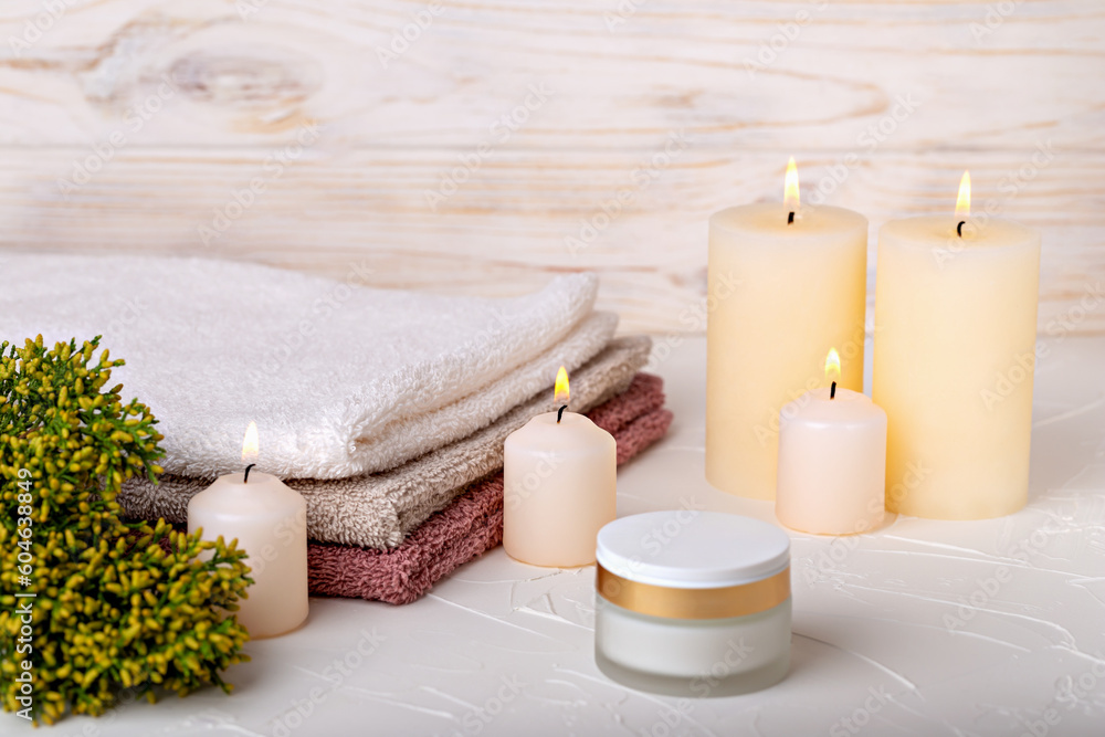 Burning candles and face cream, towels and juniper branch on light background. Concept of calmness, comfort, spa treatments. Selective focus