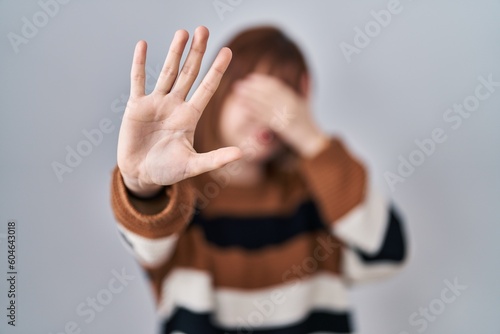 Young beautiful woman wearing striped sweater over isolated background covering eyes with hands and doing stop gesture with sad and fear expression. embarrassed and negative concept.