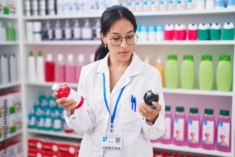 Young beautiful hispanic woman pharmacist holding medication bottles at pharmacy
