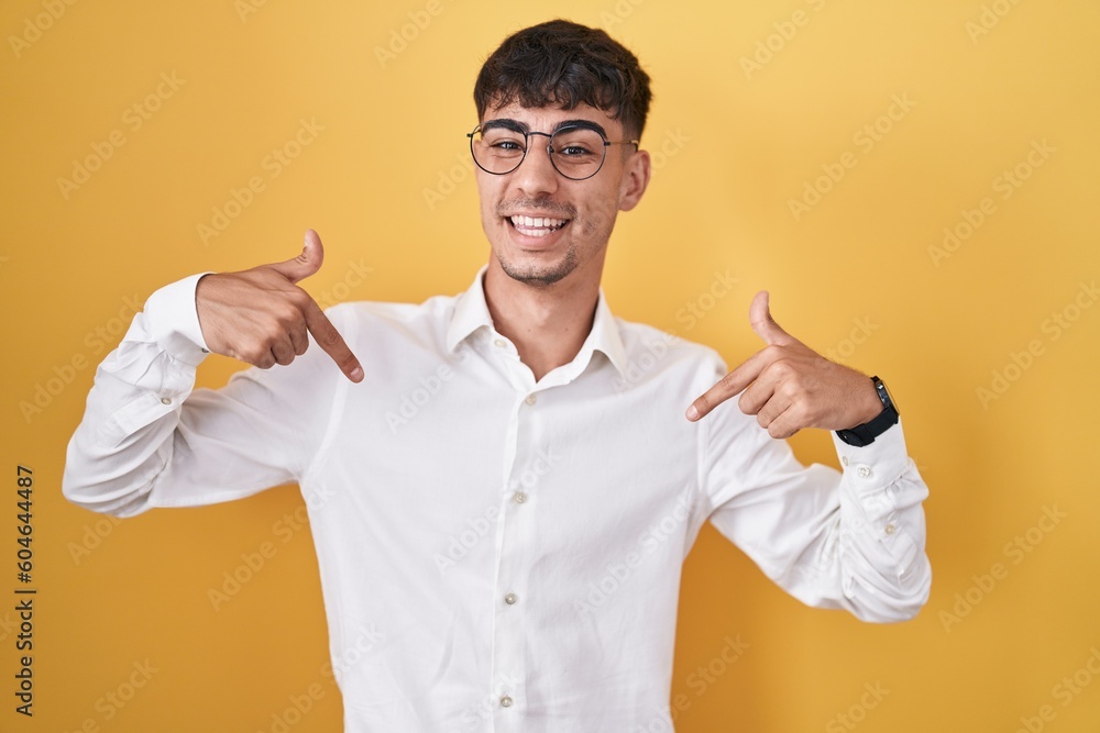 Young hispanic man standing over yellow background looking confident with smile on face, pointing oneself with fingers proud and happy. Young hispanic man standing over yellow background looking confident with smile on face, pointing oneself with fingers proud and happy.
