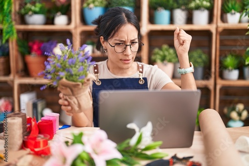 Young hispanic woman working at florist shop doing video call angry and mad raising fist frustrated and furious while shouting with anger. rage and aggressive concept. © Krakenimages.com