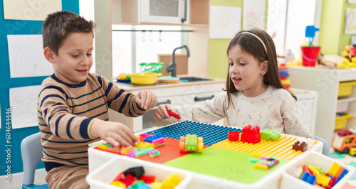 Adorable boy and girl playing with construction blocks sitting on table at kindergarten