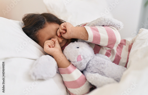 Adorable hispanic girl lying on bed waking up at bedroom