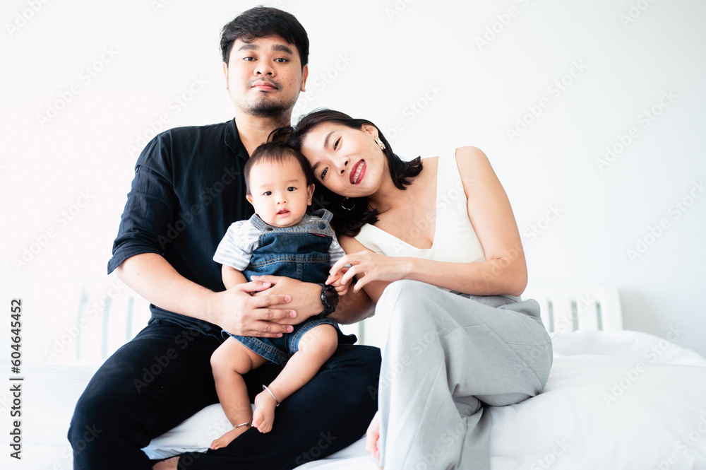Smiling Asian family in white bedroom with dad Mother and son