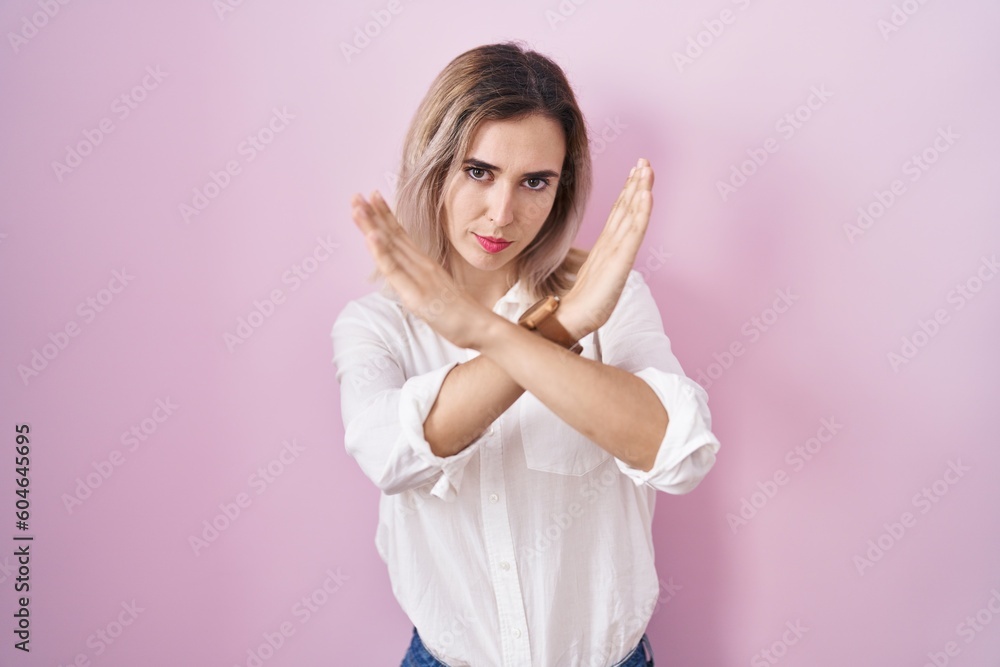 Young beautiful woman standing over pink background rejection expression crossing arms doing negative sign, angry face Young beautiful woman standing over pink background rejection expression crossing arms doing negative sign, angry face