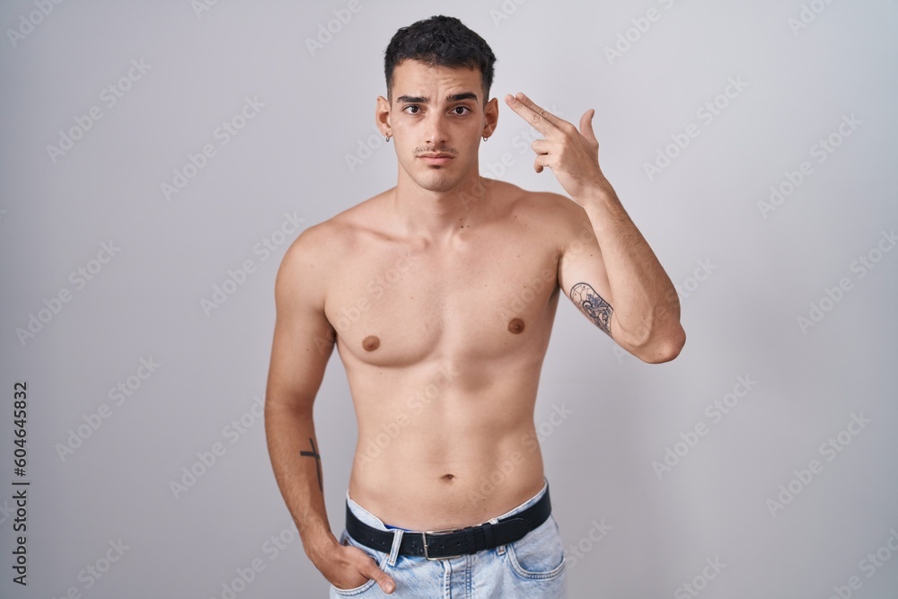 Handsome hispanic man standing shirtless shooting and killing oneself pointing hand and fingers to head like gun, suicide gesture.