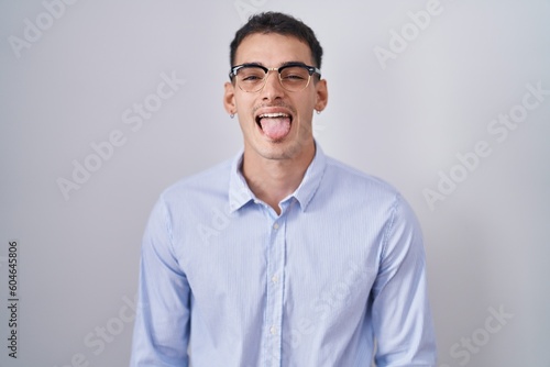 Handsome hispanic man wearing business clothes and glasses sticking tongue out happy with funny expression. emotion concept. © Krakenimages.com