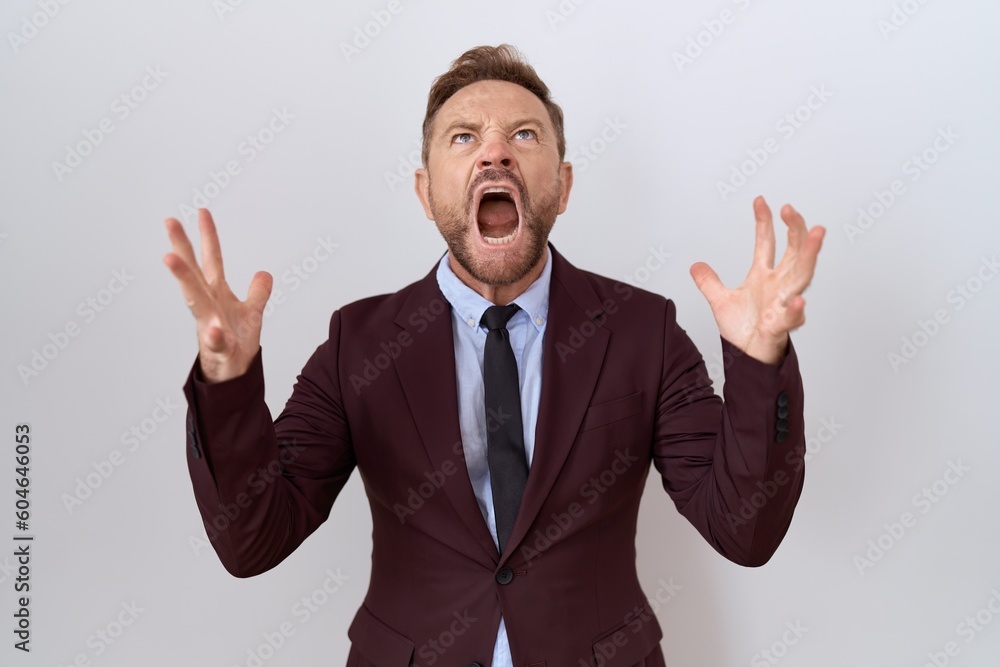Middle age business man with beard wearing suit and tie crazy and mad shouting and yelling with aggressive expression and arms raised. frustration concept. Middle age business man with beard wearing suit and tie crazy and mad shouting and yelling with aggressive expression and arms raised. frustration concept.