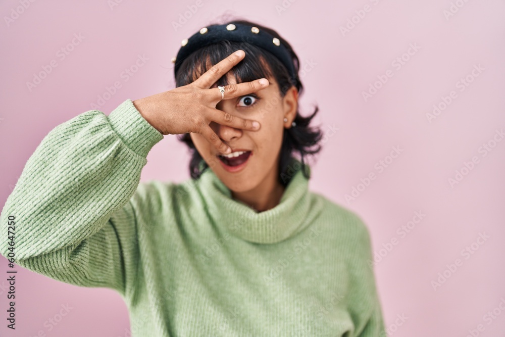 Young beautiful woman standing over pink background peeking in shock covering face and eyes with hand, looking through fingers with embarrassed expression. Young beautiful woman standing over pink background peeking in shock covering face and eyes with hand, looking through fingers with embarrassed expression.