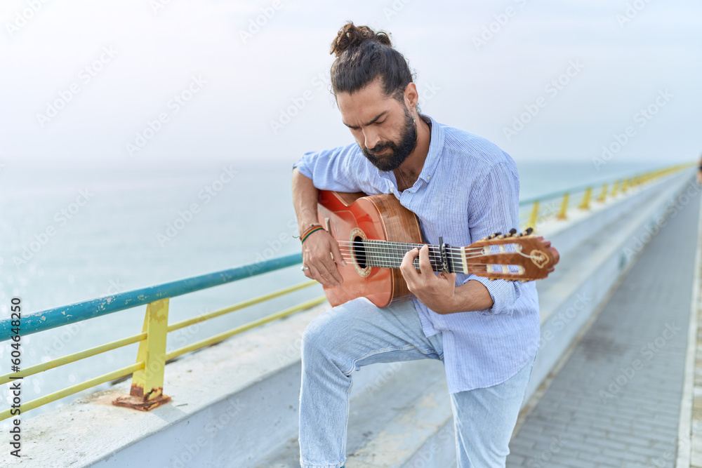 Young hispanic man musician playing classical guitar at seaside