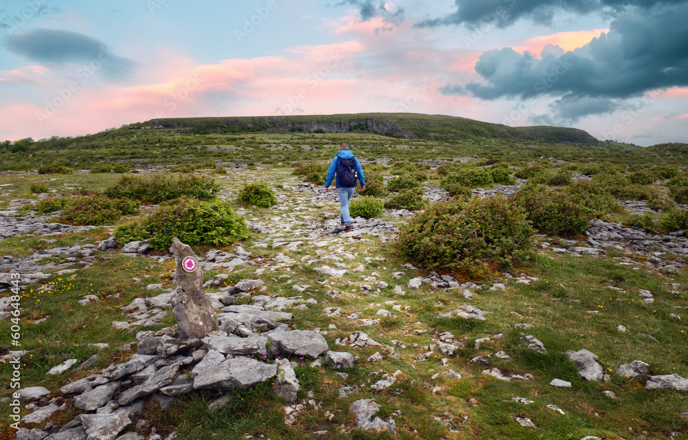 Beautiful sunrise landscape scenery with man in blue jacket hiking on top of the mountain at Lough avalla farm loop in Burren National Park, county Clare, Ireland 