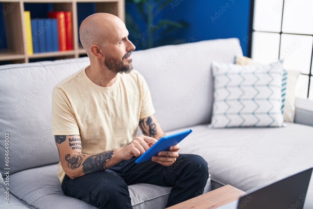 Young bald man using touchpad sitting on sofa at home