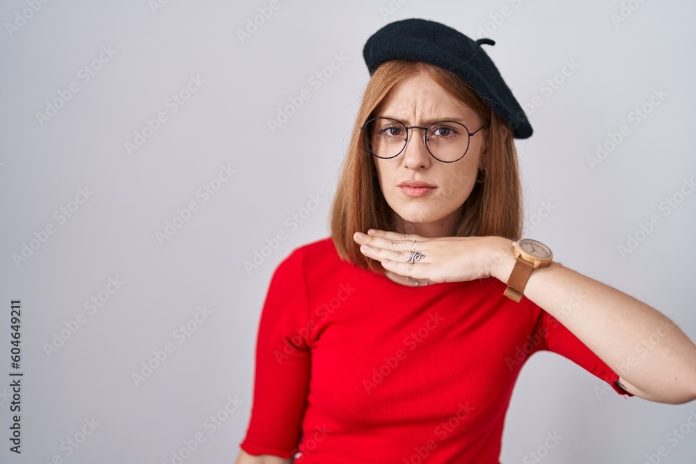 Young redhead woman standing wearing glasses and beret cutting throat with hand as knife, threaten aggression with furious violence