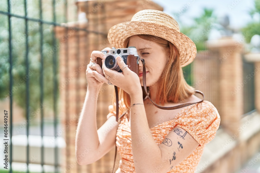 Young redhead woman tourist wearing summer hat using vintage camera at street Young redhead woman tourist wearing summer hat using vintage camera at street
