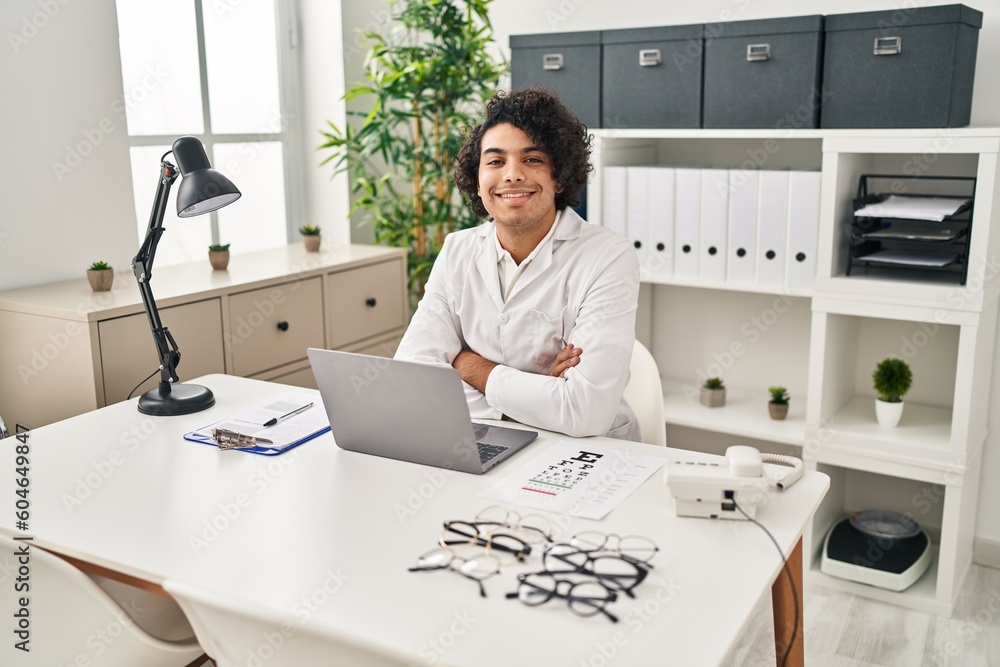 Hispanic man with curly hair working at optician office happy face smiling with crossed arms looking at the camera. positive person. Hispanic man with curly hair working at optician office happy face smiling with crossed arms looking at the camera. positive person.
