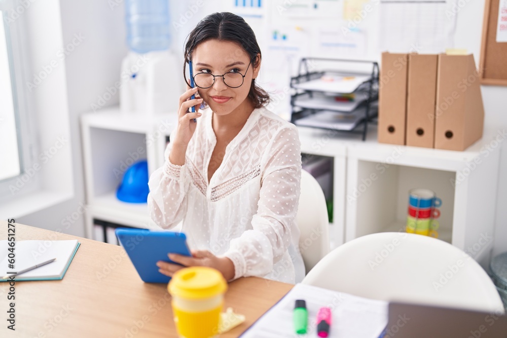 Young hispanic woman business worker talking on smartphone using touchpad at office Young hispanic woman business worker talking on smartphone using touchpad at office