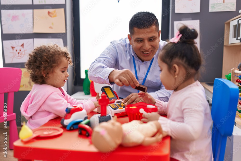 Hispanic man and girls playing supermarket game sitting on table at kindergarten Hispanic man and girls playing supermarket game sitting on table at kindergarten