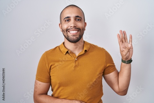 Hispanic man with beard standing over white background showing and pointing up with fingers number four while smiling confident and happy.