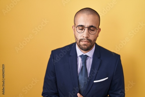 Hispanic man with beard wearing suit and tie with hand on stomach because nausea, painful disease feeling unwell. ache concept.