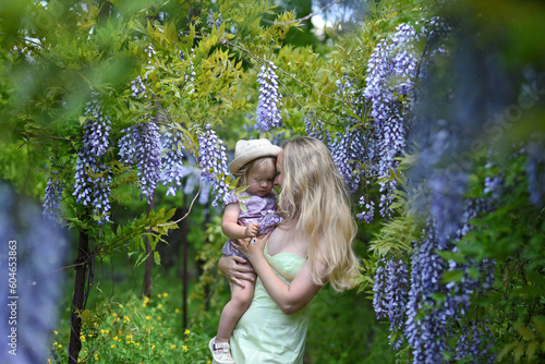 woman and her little daughter posing in spring park with wisteria flowers