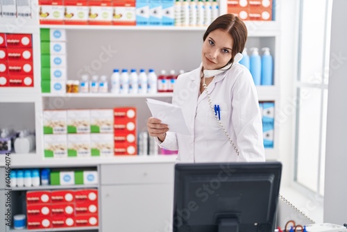 Young woman pharmacist talking on telephone working at pharmacy