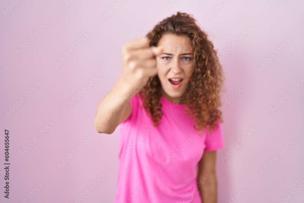 Young caucasian woman standing over pink background angry and mad raising fist frustrated and furious while shouting with anger. rage and aggressive concept. Young caucasian woman standing over pink background angry and mad raising fist frustrated and furious while shouting with anger. rage and aggressive concept.