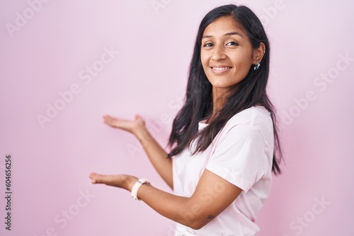 Young hispanic woman standing over pink background inviting to enter smiling natural with open hand © Krakenimages.com