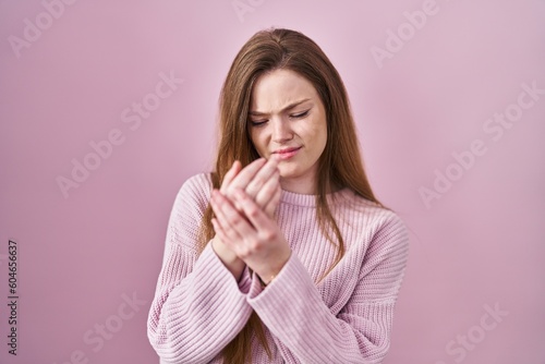 Young caucasian woman standing over pink background suffering pain on hands and fingers, arthritis inflammation