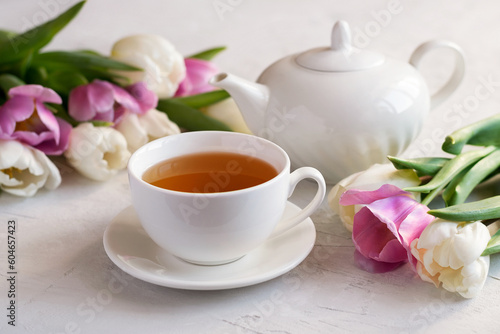 Fragrant tea in a white cup with a teapot and a bouquet of fresh tulips on a bright table. The concept of tea. Close-up. Selective focus.