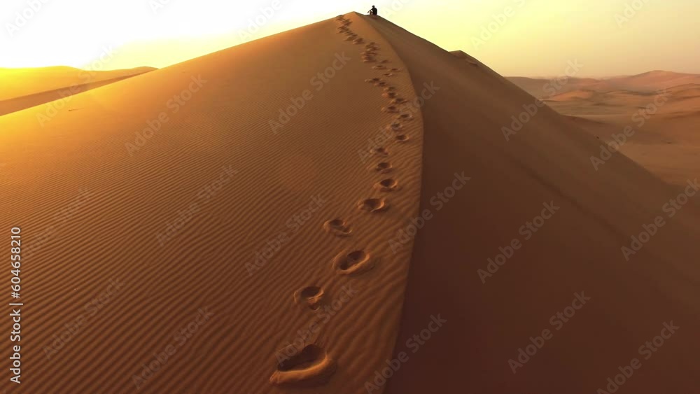 Travel, drone and footsteps with man in desert for hiking, adventure and freedom. Sunset, discover and expedition hobby with person thinking on sand dune hill for explorer, vacation and journey