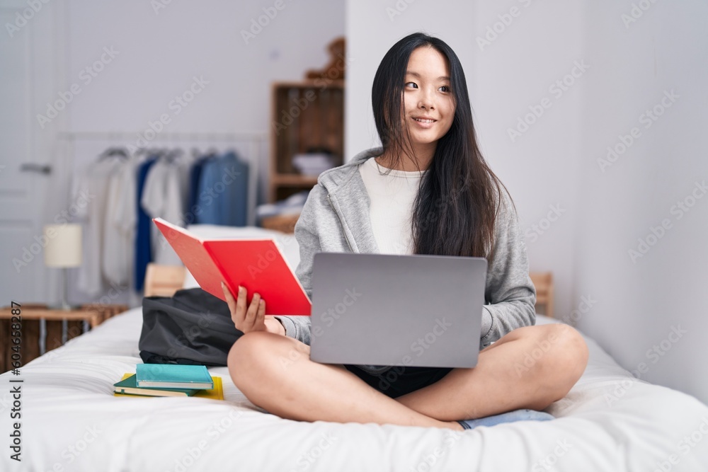 Young chinese woman using laptop reading notebook studying on bed at bedroom Young chinese woman using laptop reading notebook studying on bed at bedroom