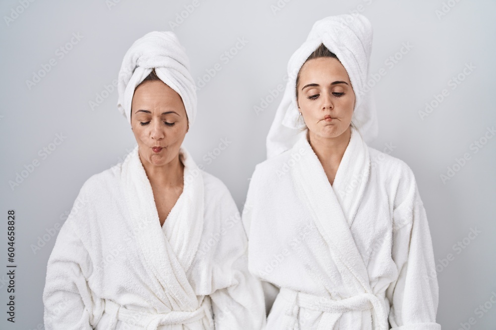 Middle age woman and daughter wearing white bathrobe and towel making fish face with lips, crazy and comical gesture. funny expression. Middle age woman and daughter wearing white bathrobe and towel making fish face with lips, crazy and comical gesture. funny expression.