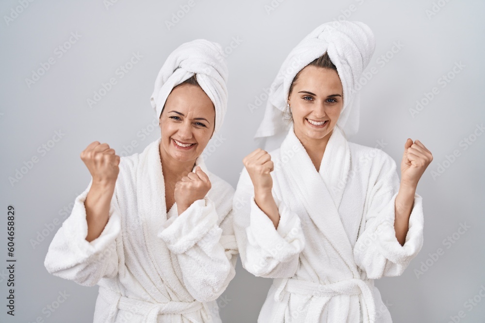Middle age woman and daughter wearing white bathrobe and towel very happy and excited doing winner gesture with arms raised, smiling and screaming for success. celebration concept. Middle age woman and daughter wearing white bathrobe and towel very happy and excited doing winner gesture with arms raised, smiling and screaming for success. celebration concept.