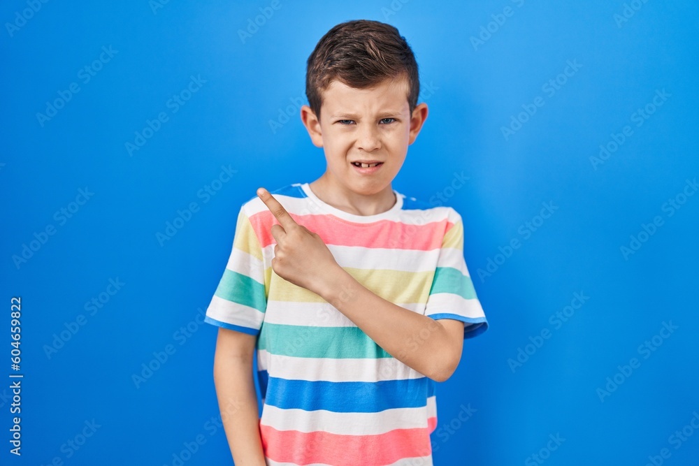 Young caucasian kid standing over blue background pointing aside worried and nervous with forefinger, concerned and surprised expression Young caucasian kid standing over blue background pointing aside worried and nervous with forefinger, concerned and surprised expression