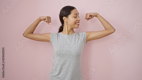 Young beautiful hispanic woman smiling wearing sportswear showing arm muscles over isolated pink background