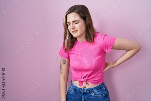 Blonde caucasian woman standing over pink background suffering of backache, touching back with hand, muscular pain