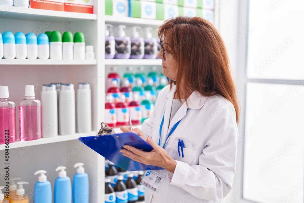 Middle age woman pharmacist writing on document at pharmacy