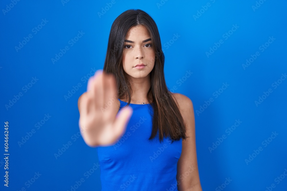 Fototapeta premium Hispanic woman standing over blue background doing stop sing with palm of the hand. warning expression with negative and serious gesture on the face.