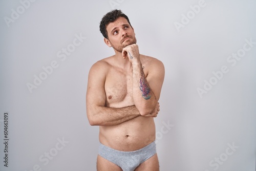 Obraz na plátně Young hispanic man standing shirtless wearing underware with hand on chin thinking about question, pensive expression