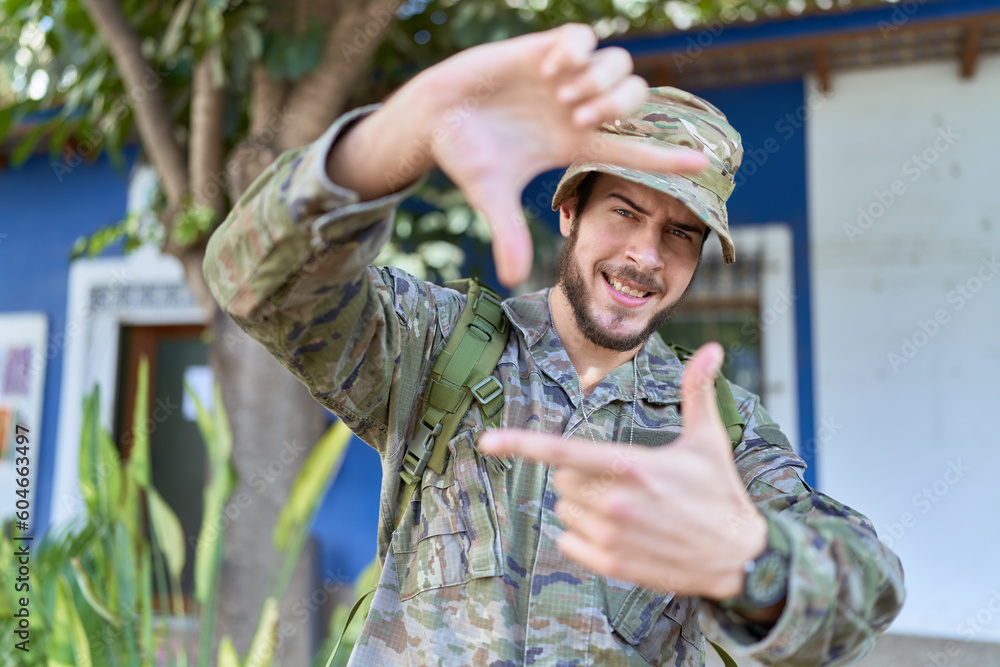 Young hispanic man wearing camouflage army uniform outdoors smiling making frame with hands and fingers with happy face. creativity and photography concept.