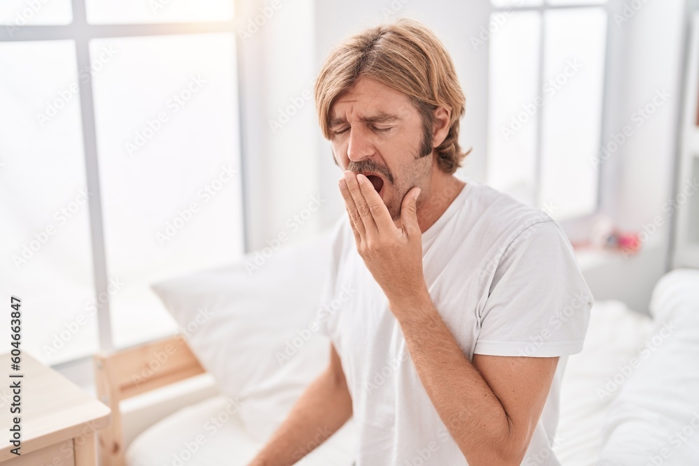 Young blond man sitting on bed yawning at bedroom Young blond man sitting on bed yawning at bedroom